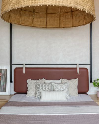 Bedroom with large woven pendant lamp over a tan leather headboard and layered cushions