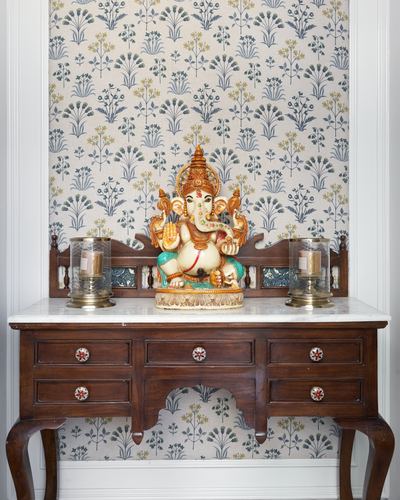 carved Ganesh idol on marble-topped wooden console against floral wallpaper