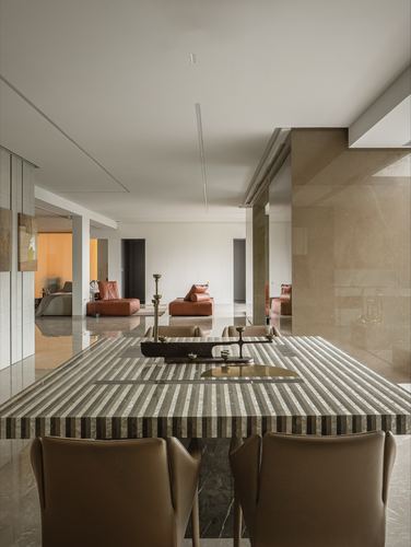 Striped stone dining table with leather chairs opening onto a living room with terracotta sofas