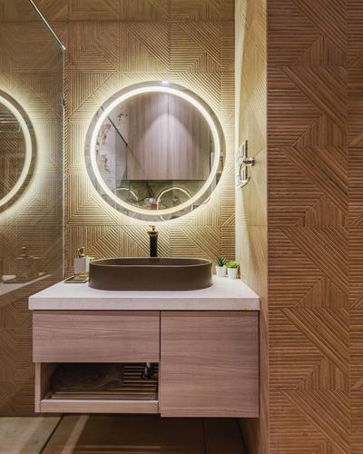 Round backlit mirror above stone vessel sink on floating wood vanity in textured bathroom