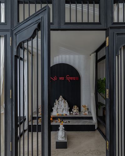 Black wooden grille doors open onto a marble pooja niche with white deity idols and red script