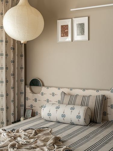 Bedroom corner with round paper pendant, patterned headboard, and framed art on beige wall