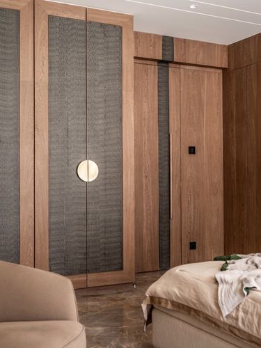 Wood-panelled bedroom wardrobe wall with textured grey inserts and circular brass handle