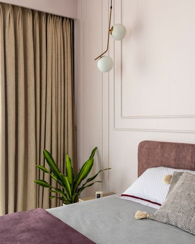 Blush pink paneled bedroom corner with brass globe pendant, mauve headboard, and beige curtains