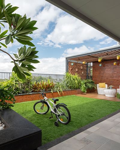 Rooftop terrace with artificial lawn, child's bicycle, brick wall and terracotta jaali screen under open sky