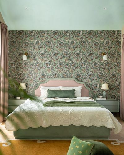 Bedroom with green floral wallpaper, pink velvet headboard, green bed frame and mustard rug