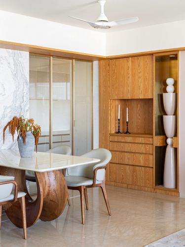 Dining area with marble-top table on carved wood base, wooden cabinetry, and sculptural vases