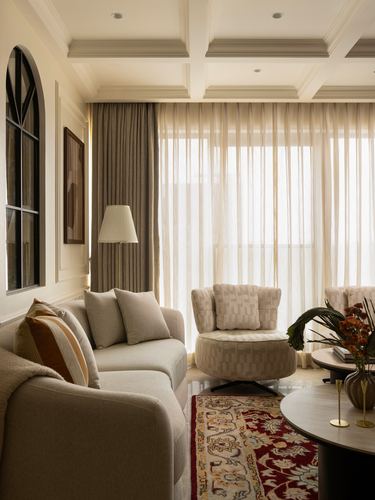 Beige living room with coffered ceiling, sheer curtains, round swivel chair and red patterned rug