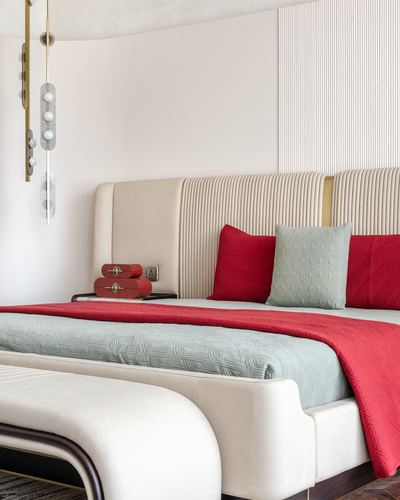 Bed with cream tufted headboard, red and sage cushions, brass pendant lights beside