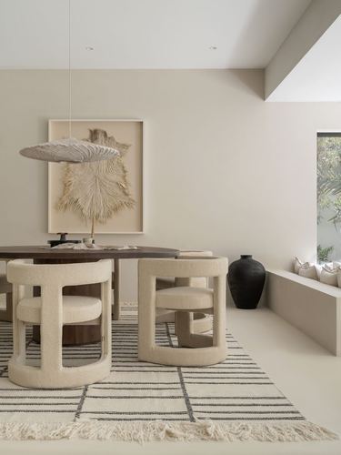 Neutral dining room with round wood table, boucle barrel chairs, feather pendant, and black vase
