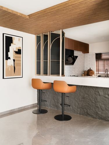 Kitchen counter with two orange bar stools beneath arched glass cabinets and wood ceiling