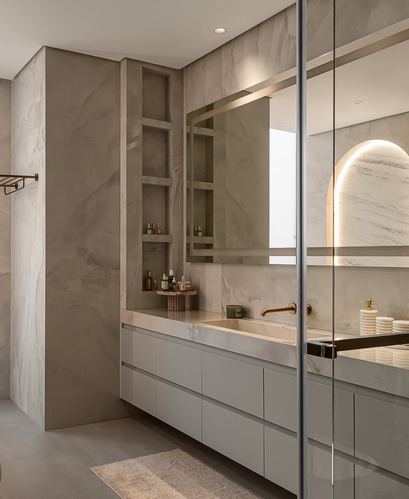 Marble bathroom with floating grey vanity, framed mirror, and backlit arched niche seen through glass shower door