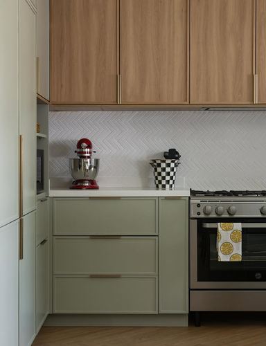 Kitchen corner with wood upper cabinets, sage-green lower drawers, herringbone tile backsplash, and gas range