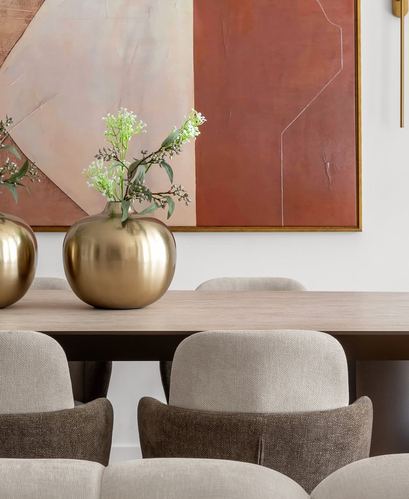 Dining table with brass vases and greenery beneath a terracotta abstract painting