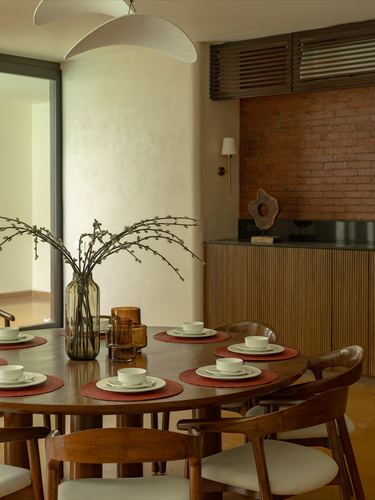 Round wood dining table set with white bowls before an exposed brick wall and fluted cabinet.