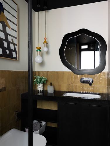 Bathroom with mustard zellige tile, black vanity, and a wavy black mirror