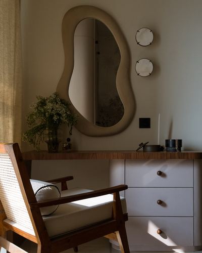 Cane armchair beside dresser with curved mirror and round wall sconces in warm light
