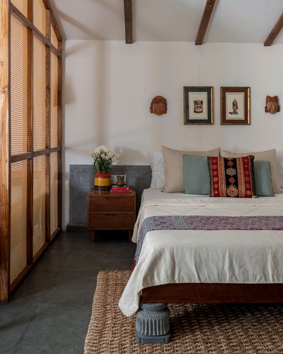 Bedroom with exposed teak rafters, layered textiles, tribal masks and a jute rug