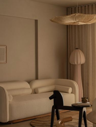 Beige curved sofa in muted living room with woven pendant light and black horse toy