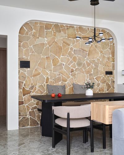 Dining nook with black table under arched stone-clad wall and sculptural chandelier