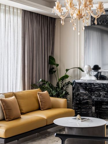 Mustard leather sofa beside black marble fireplace under a crystal chandelier in a neutral living room