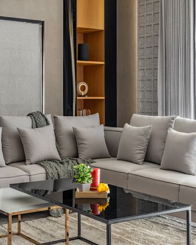 Grey sectional sofa with cushions beside a black glass coffee table and wood display niche