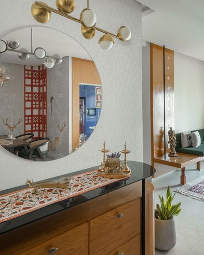 Foyer console with round mirror reflecting dining room, brass chandelier, wooden partition beyond