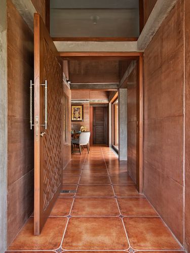 Open carved wooden door leading through a terracotta-tiled corridor into a dining area beyond