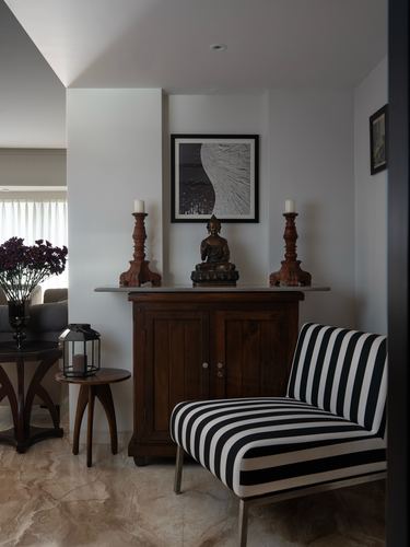 Entry vignette with wooden cabinet, buddha statue, candle stands and striped chair on marble floor