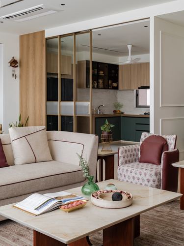 Living room with beige sofa, marble coffee table, and glimpse into green kitchen through glass sliders