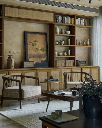 Living room with wooden bookshelf, cane cabinets, framed artwork niche, and two curved wooden armchairs