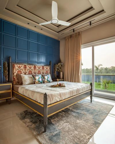 Bedroom with blue panelled wall, patterned headboard bed, and glass door to garden at sunrise
