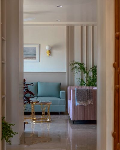 View through doorway into living room with sage sofa, pink armchair, and fluted panelled wall