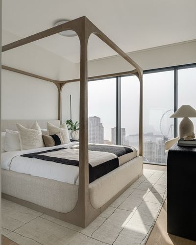 Neutral bedroom with wooden four-poster bed frame overlooking a hazy Dubai skyline through floor-to-ceiling windows