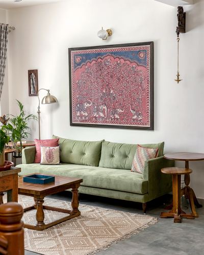 Sage green velvet sofa beneath a large pink and blue tapestry with wooden side tables