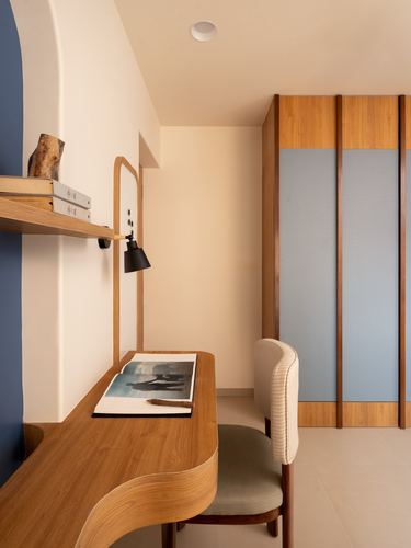 Curved wooden desk with black sconce beside blue-paneled wardrobe in study nook