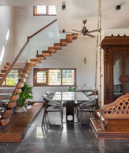 Dining area under floating staircase with carved wood cabinet and hanging swing, Bangalore villa