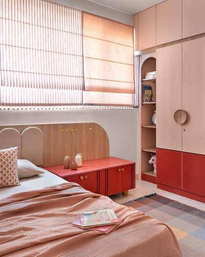 Child's bedroom with scalloped headboard, red cabinet, and arched wardrobe niche in coral tones