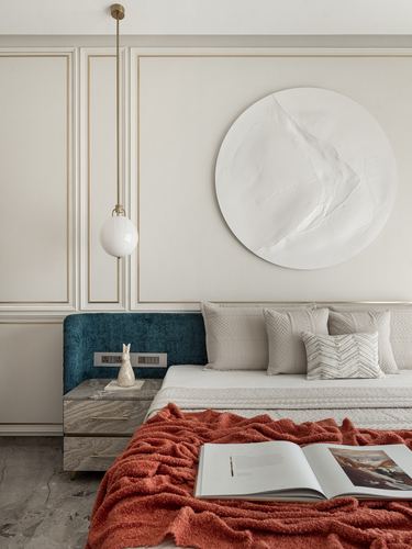 Bedroom corner with teal headboard, terracotta throw, and round textured plaster wall art above bed