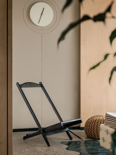 Black folding cane chair beneath round wall clock in neutral alcove with terrazzo floor