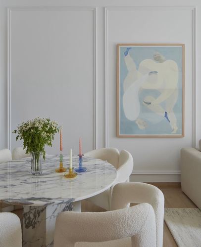 Round marble dining table with cream boucle chairs beneath a framed figurative artwork on paneled wall