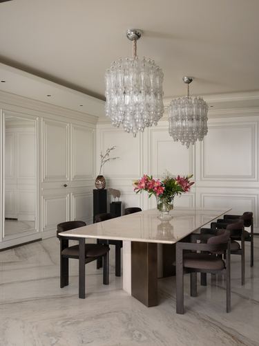 Formal dining room with marble table, dark upholstered chairs, and two tiered glass chandeliers
