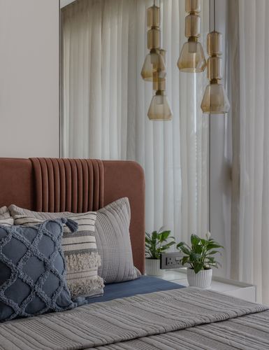 Terracotta channel-tufted headboard with layered cushions beneath amber glass pendant lights and sheer curtains