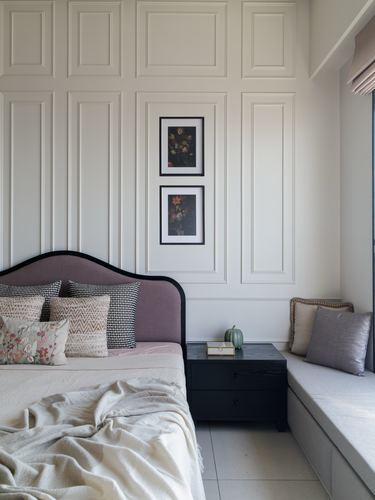 Bedroom with mauve upholstered headboard, paneled wall, framed floral art, and window seat bench