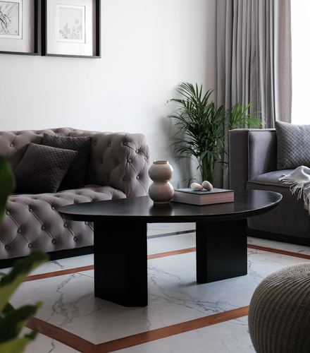 Grey tufted sofas around a black round coffee table on marble floor with inlay border