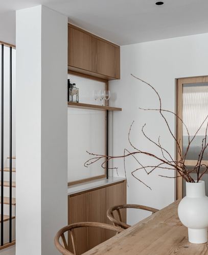 White dining nook with wooden cabinetry, open bar shelf, and table set with dried branches in a vase