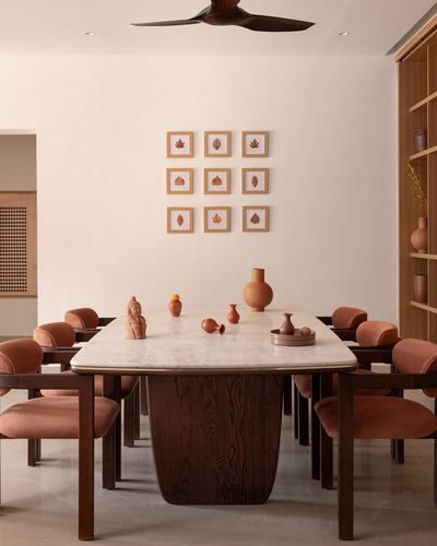 Dining room with marble-top table on wood pedestal, terracotta chairs, and framed leaf art