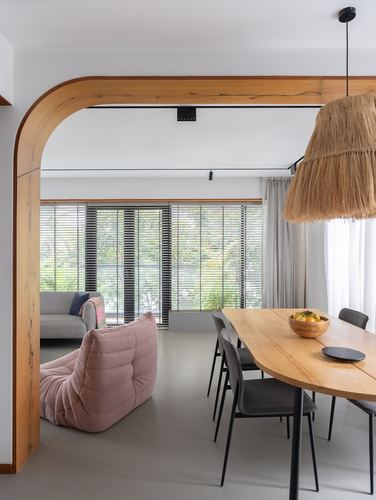 Dining table under raffia pendant light beside pink sofa and wood archway to living room