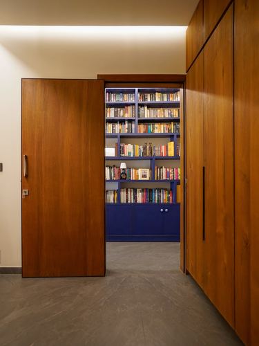 Wooden pivot door opens onto a blue bookshelf-lined library room