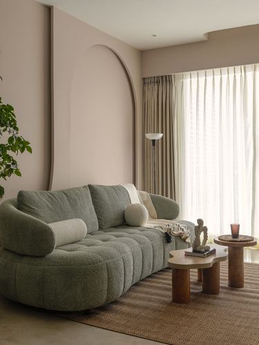 Curved sage green boucle sofa against a blush arched wall niche with wood coffee tables and sheer curtains.